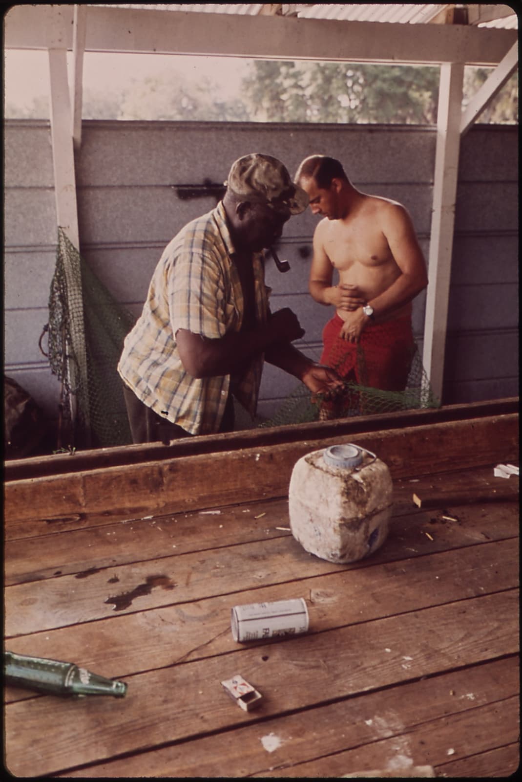 Two men mending a shrimp net in a wooden shed by the water