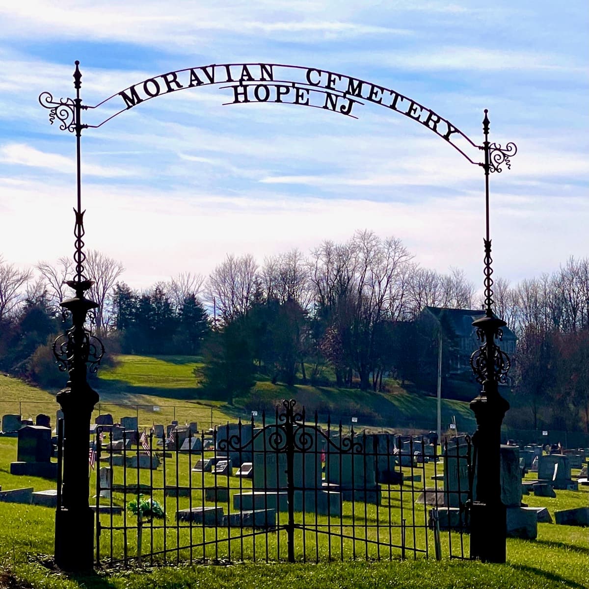 An iron and stone gateway at the edge of a cemetery