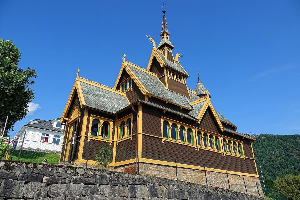 A dark wooden church with steep roofs and a slender spire among trees
