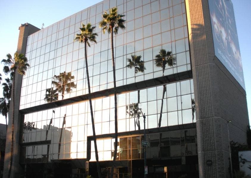 A glass-fronted office building with palm trees in front