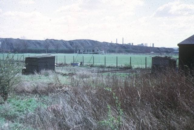 A long grey ridge of spoil heaps behind fields and fences