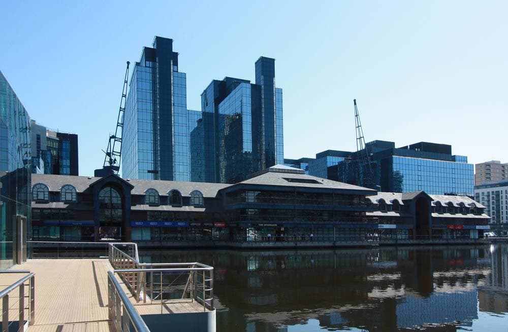 Dock water with glass office towers and a timber-clad building on the far side