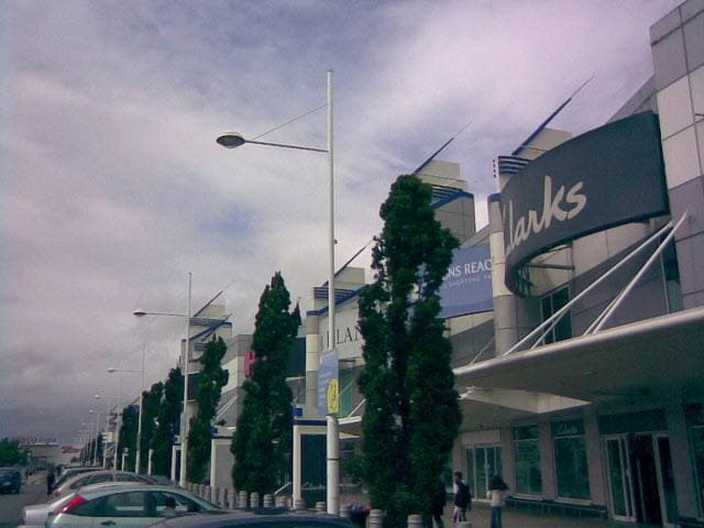 A row of shop fronts and young trees along a car park