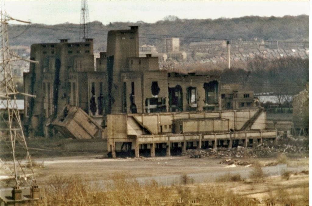 Broken concrete gasworks buildings with gaping walls under a grey sky