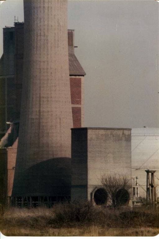A tall round brick chimney beside a low concrete building