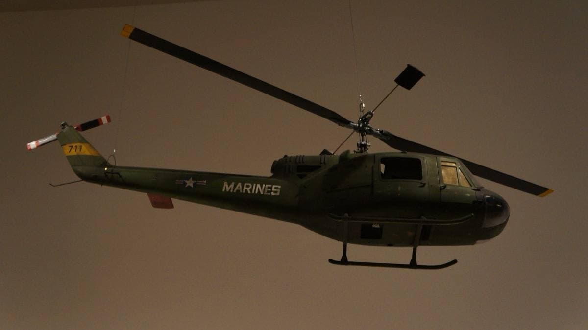 A dark green model helicopter marked MARINES hanging against a dark wall