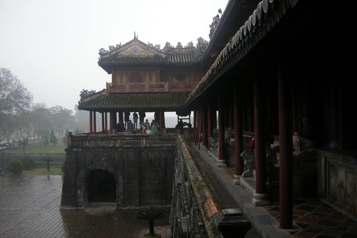 A two-tier wooden pavilion with curved tiled roofs on a stone gate, in mist