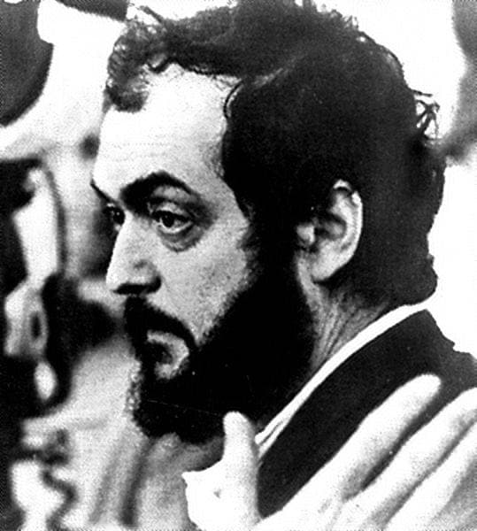 Stanley Kubrick in black and white, bearded, in profile with a hand raised to his face