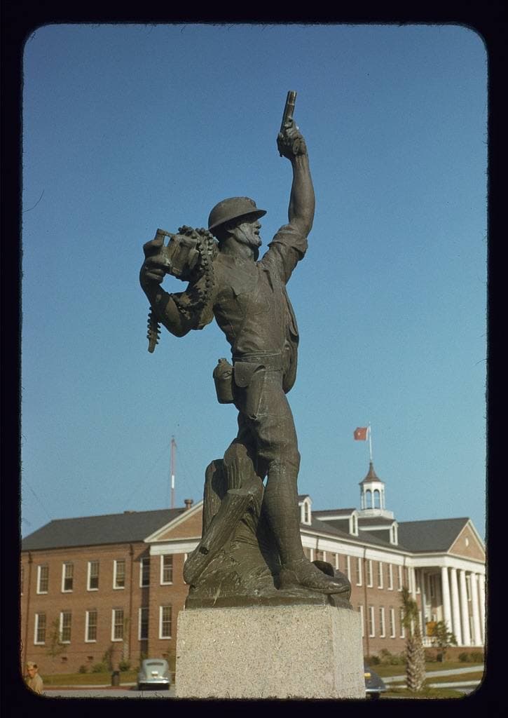 A bronze statue of a Marine on a plinth in front of a brick building