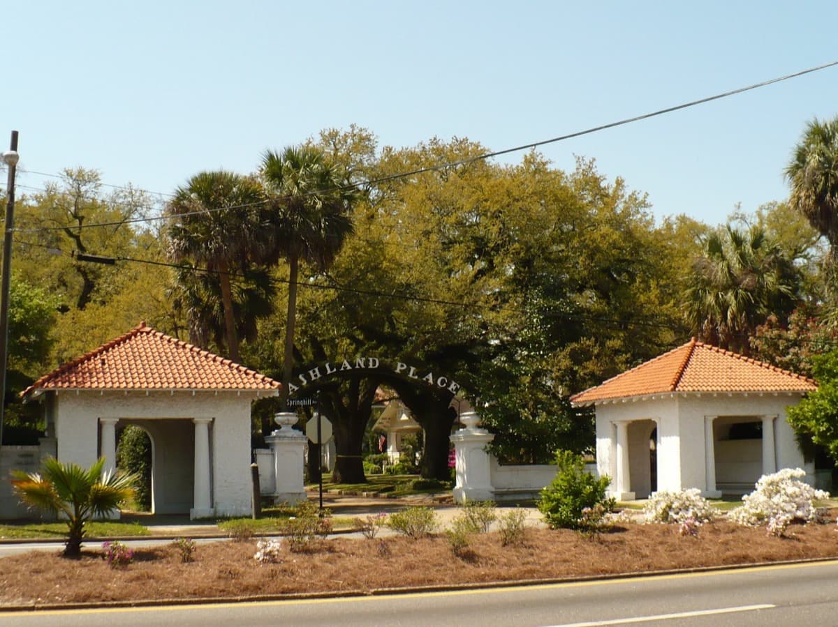 A street entrance between stone gateposts leading into a tree-lined residential district