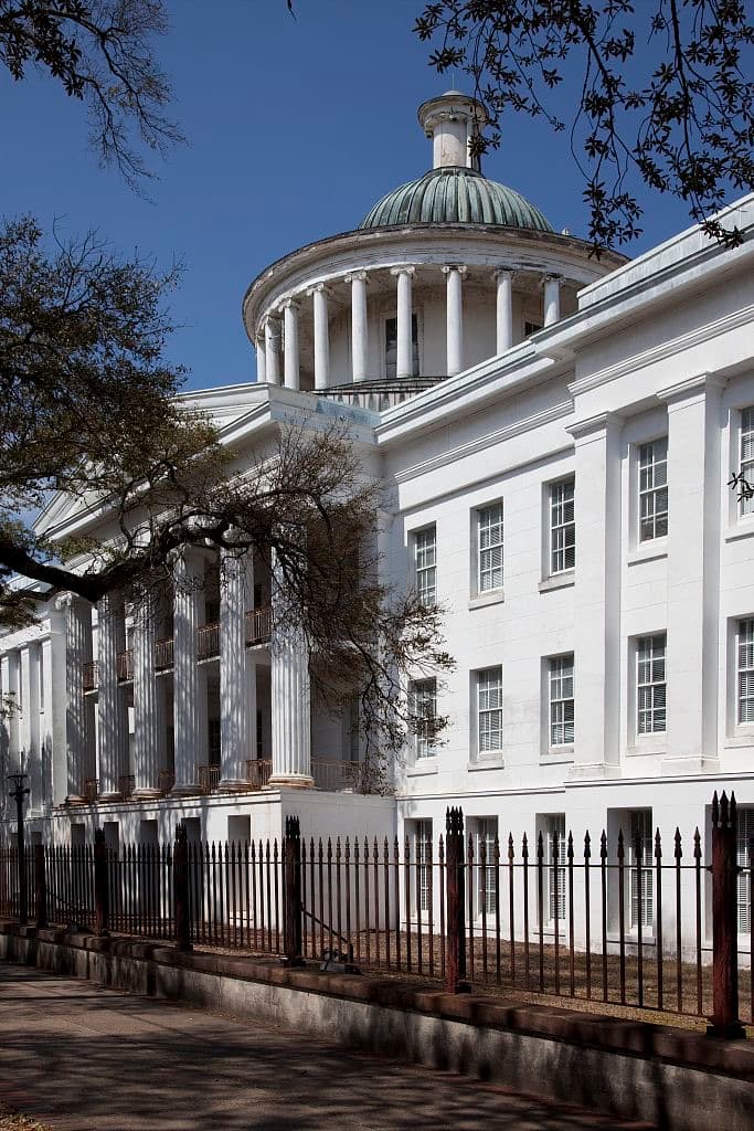 A white Greek Revival school building with a tall columned portico behind a lawn