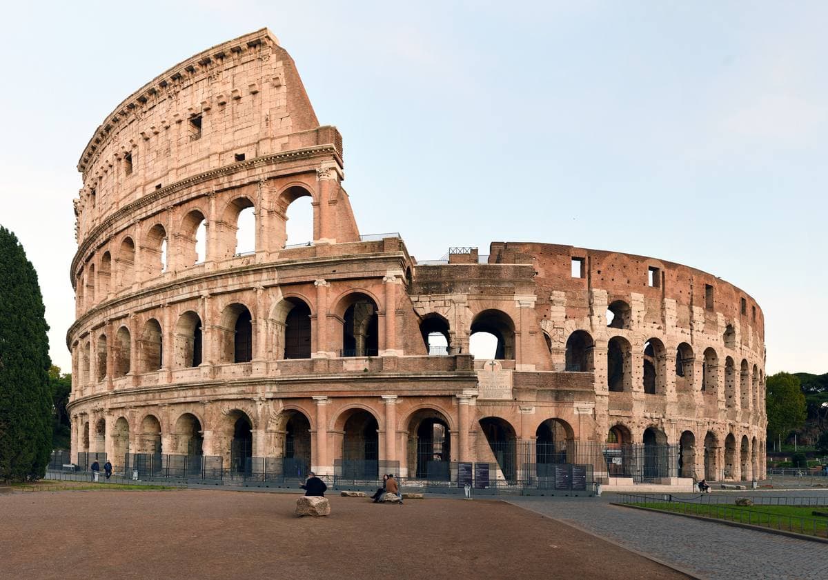 The Colosseum’s curved arcades of travertine under a pale blue sky