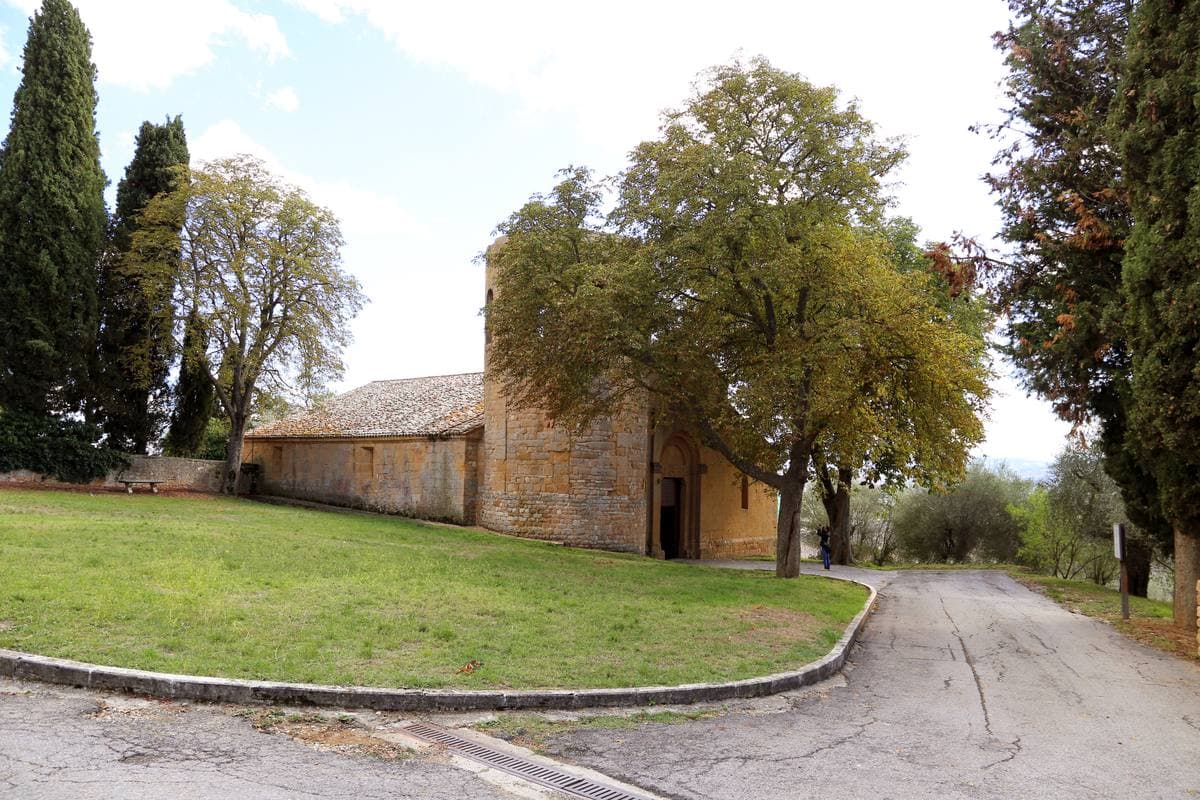 A small Romanesque stone church among trees beside a curving lane