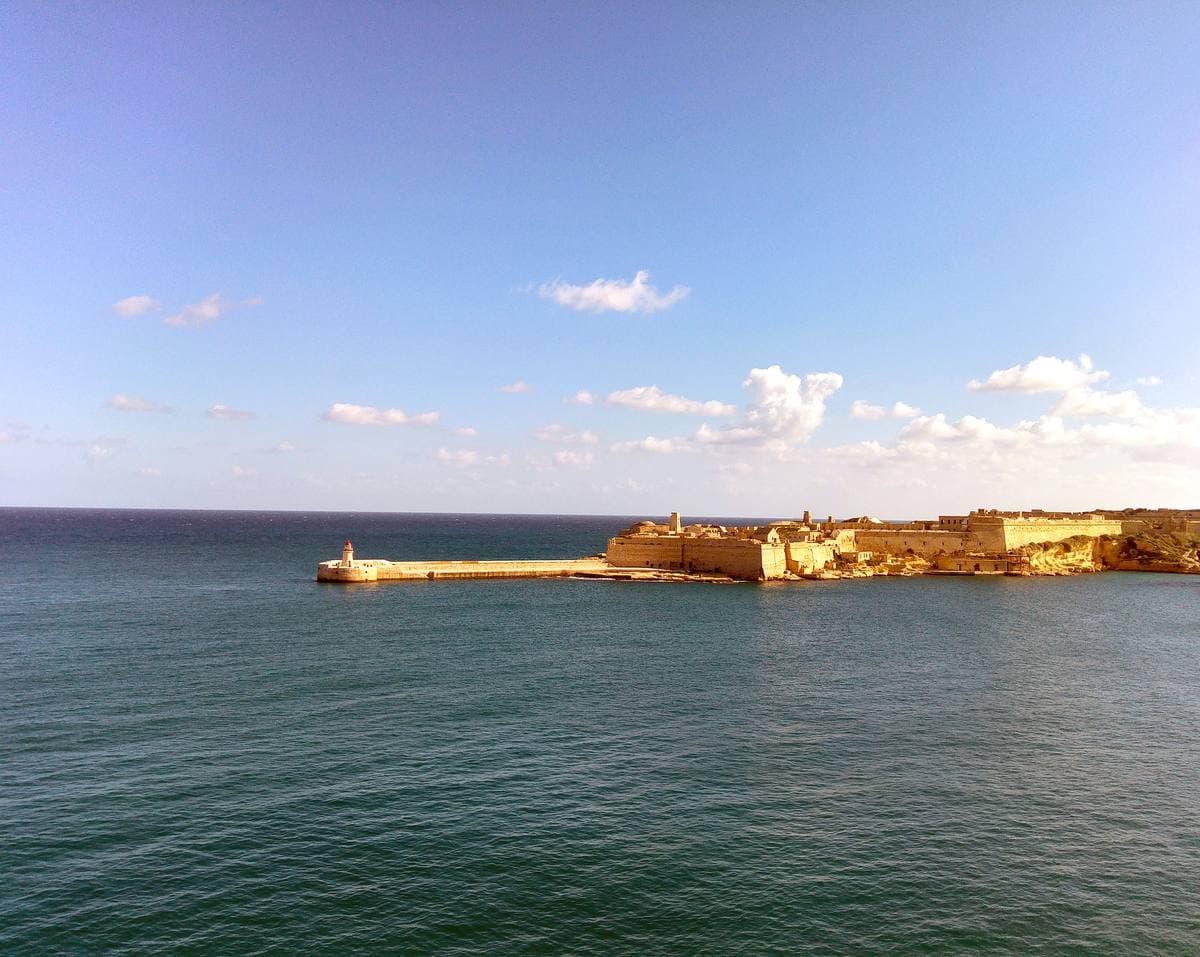 A long honey-coloured stone fort on a low headland over a blue sea, with a breakwater in front