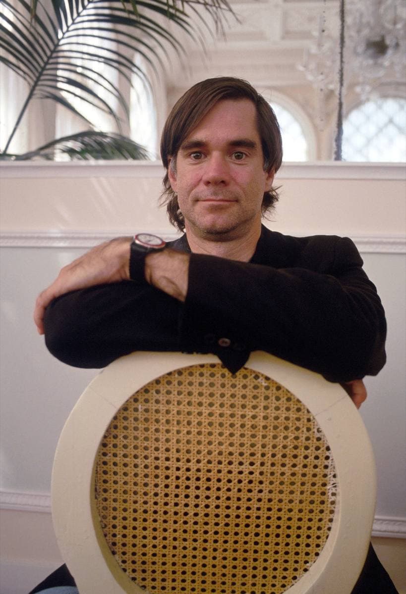Gus Van Sant leaning on the back of a cane chair