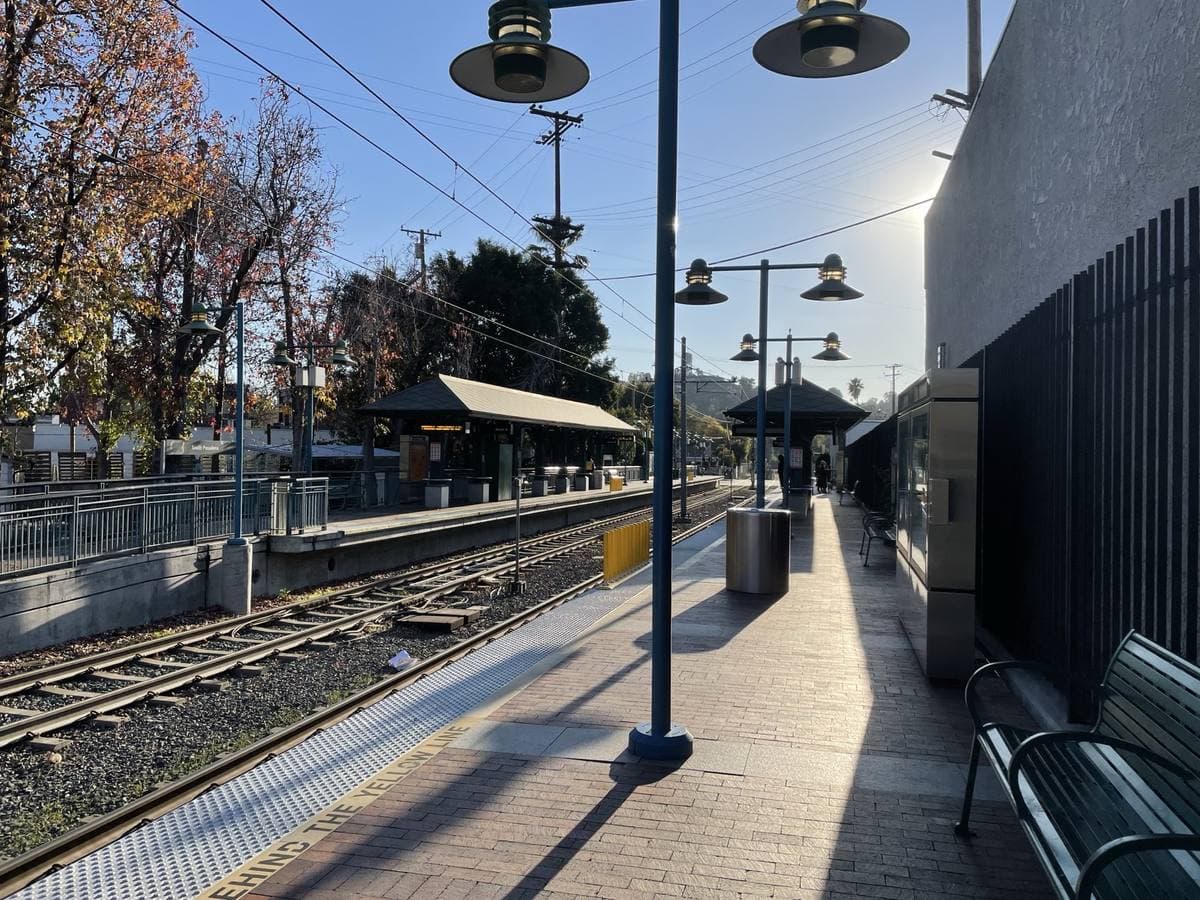 A light-rail platform with lamps and benches beside the tracks, autumn-coloured trees beyond