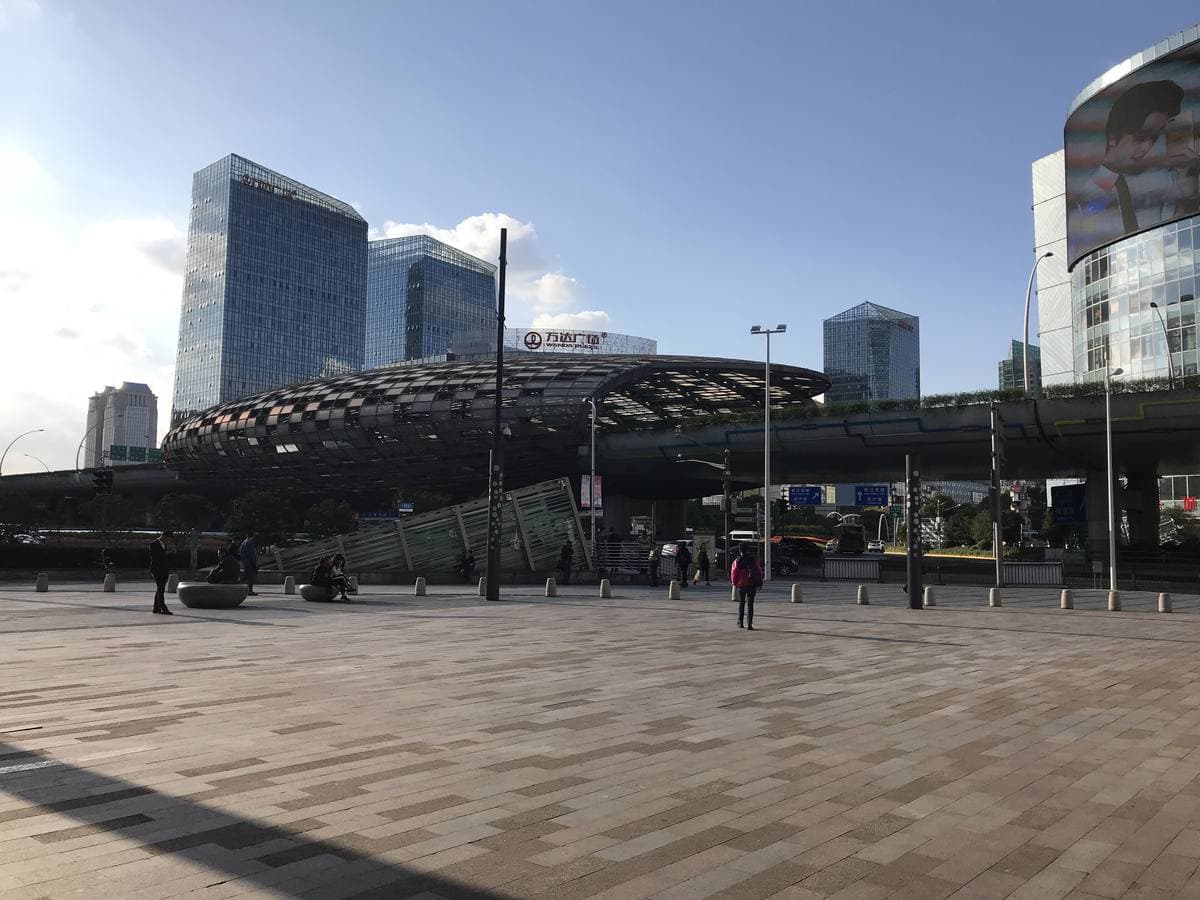 A wide paved square with glass towers and a raised road behind