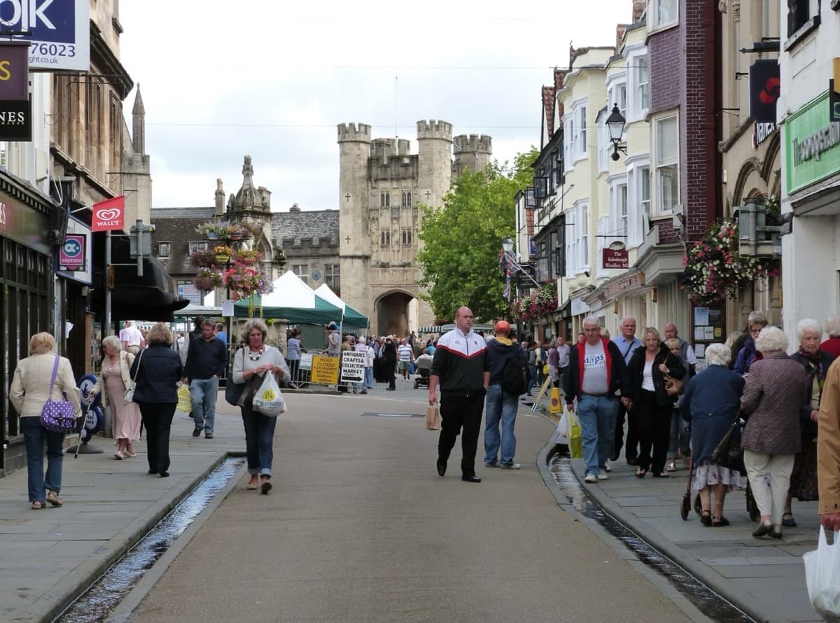 A town high street with shops and parked cars
