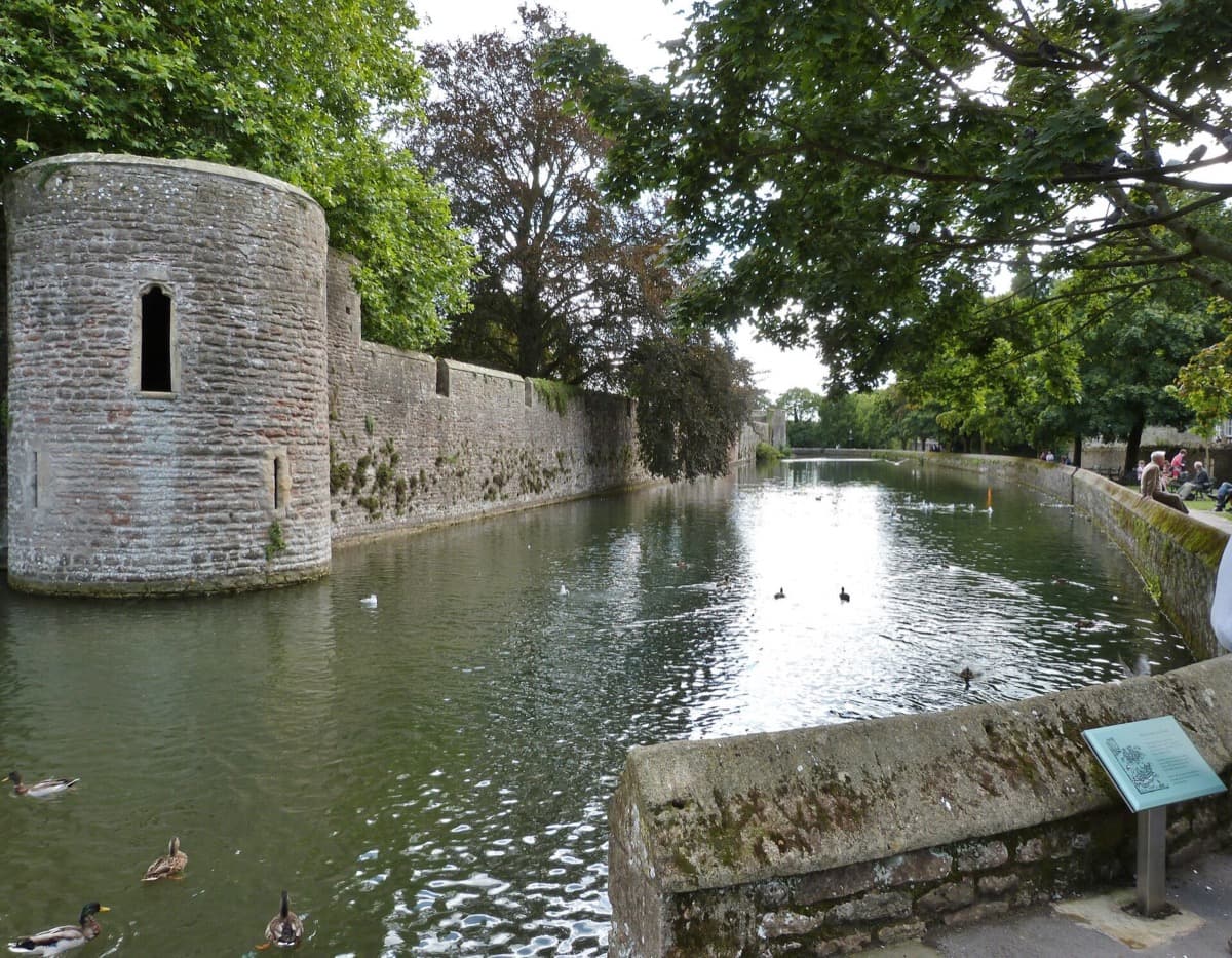 A moat in front of a fortified stone wall and gatehouse