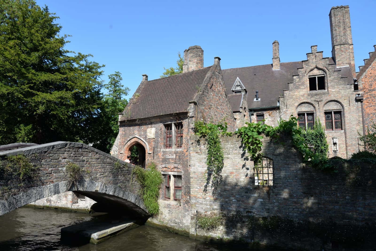 A small stone footbridge over a canal beside an ivy-covered brick house