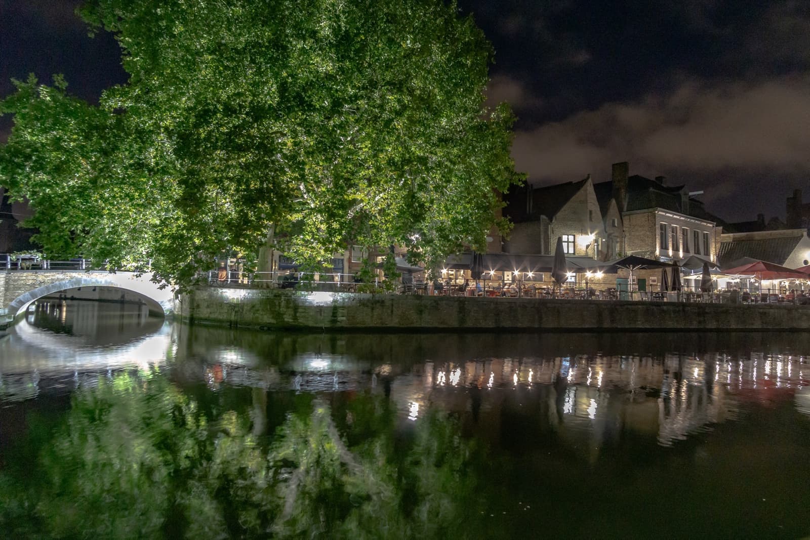 A lit bridge and houses reflected in a dark canal