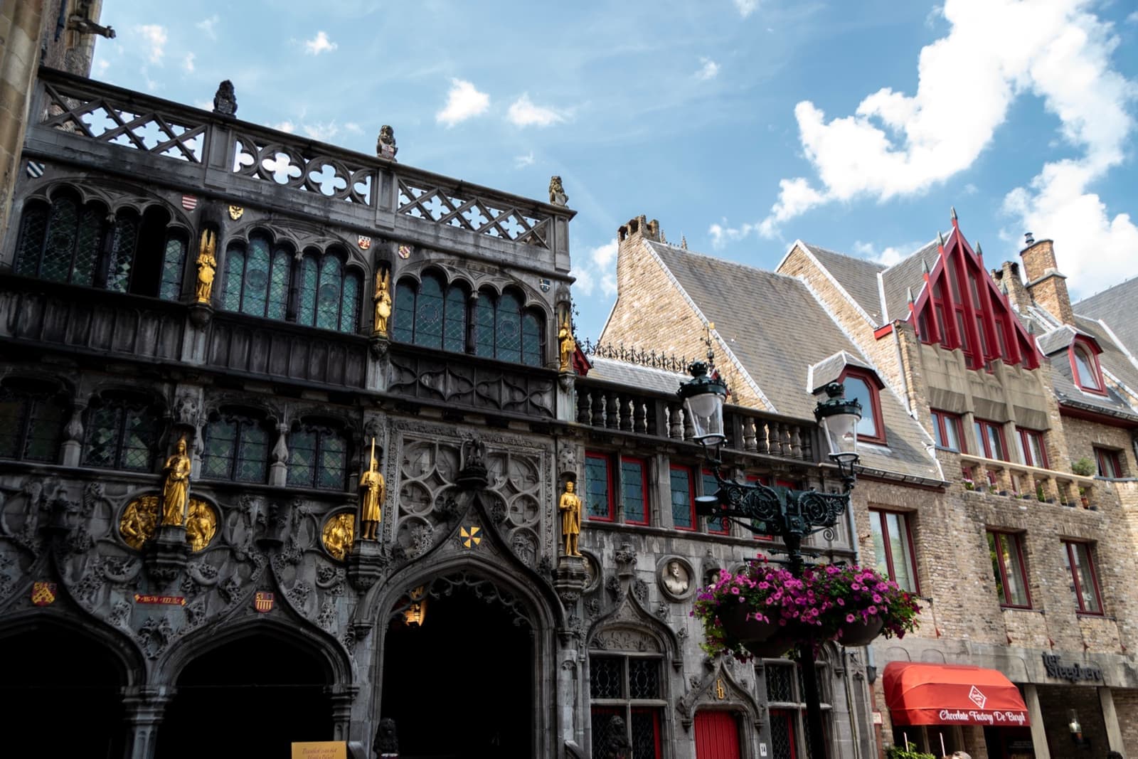 An ornate late-Gothic facade with gilded statues beside stepped-gable houses