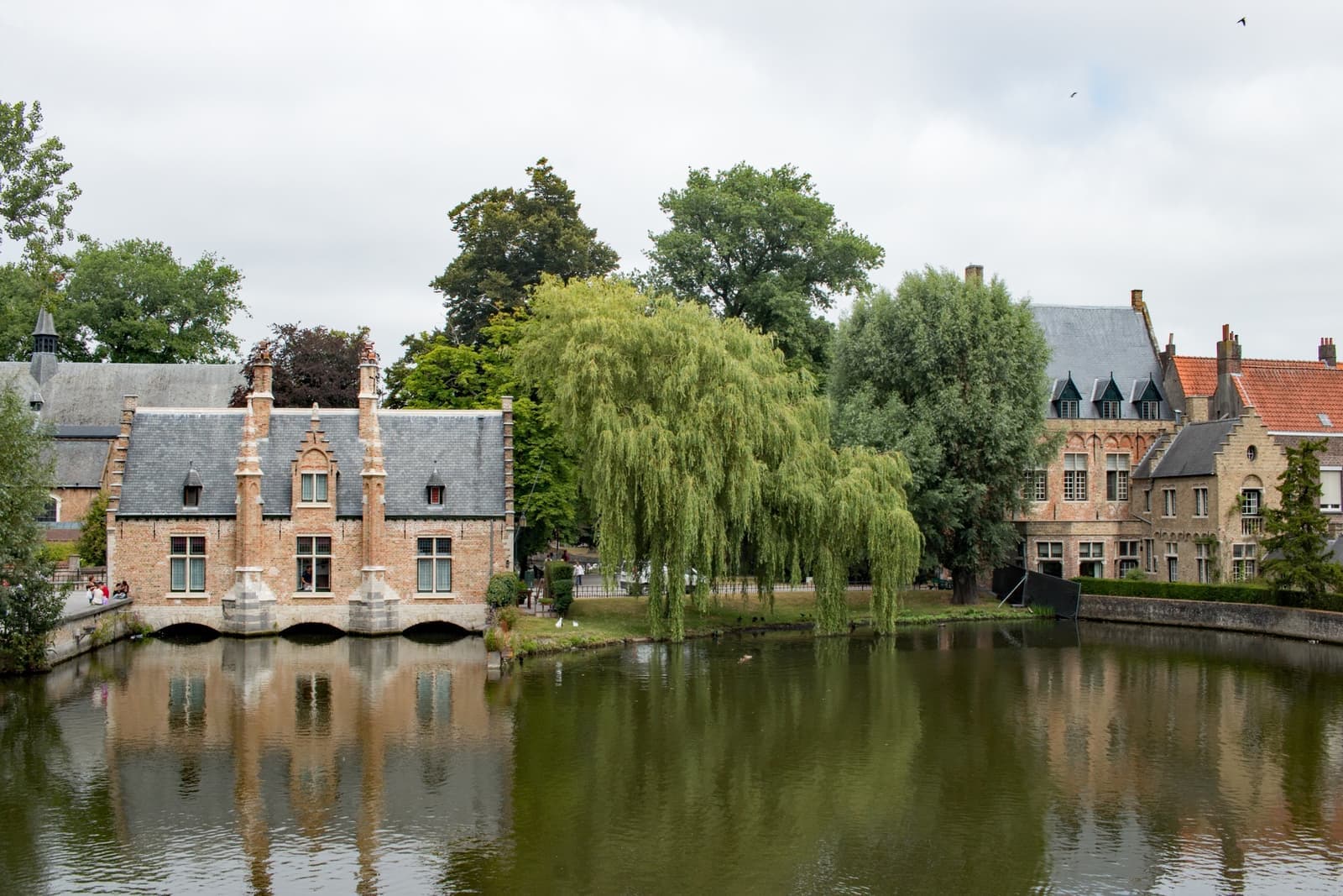 A still lake with willows and brick buildings on the far bank