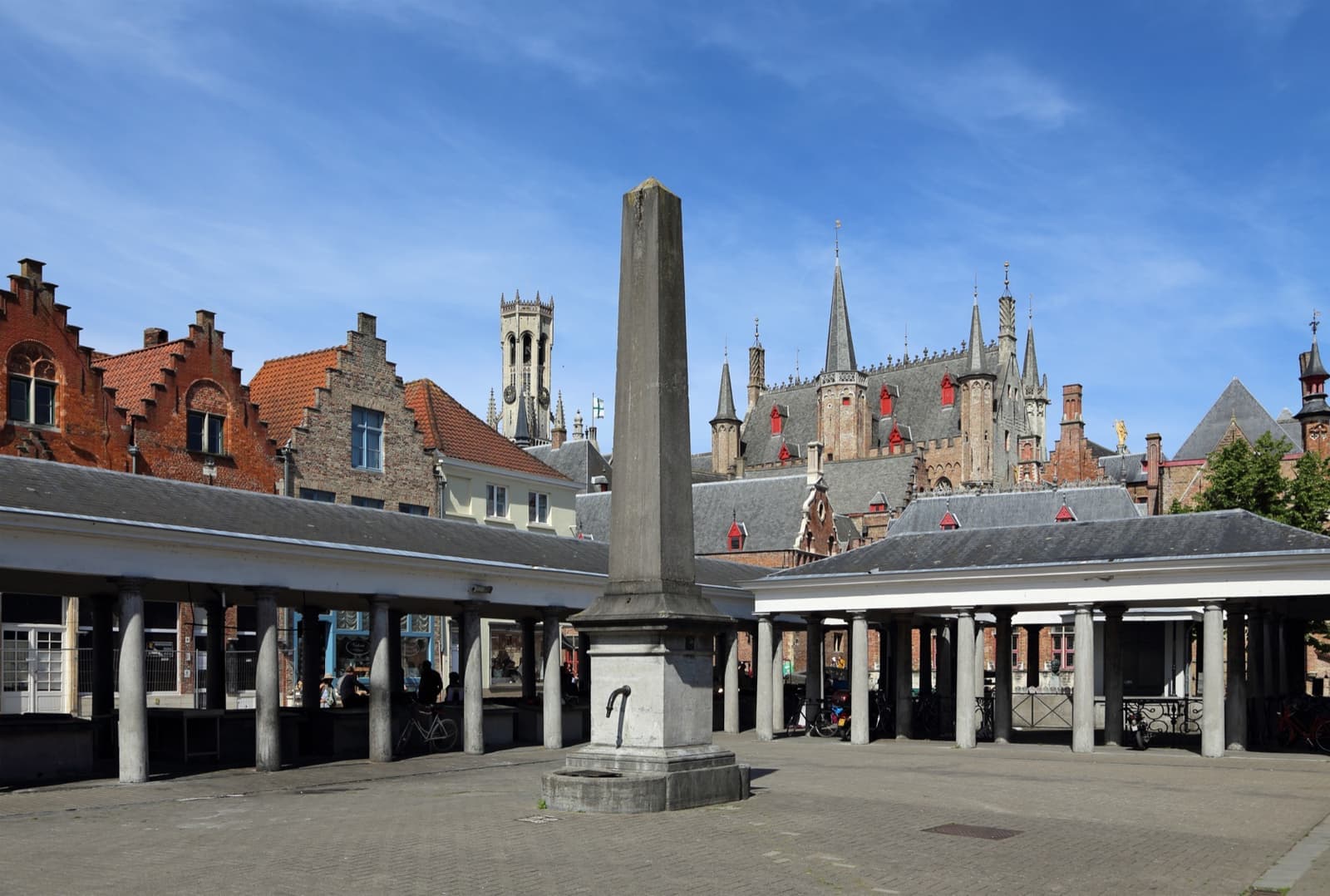 A classical colonnade around a square with an obelisk pump, the Belfry beyond