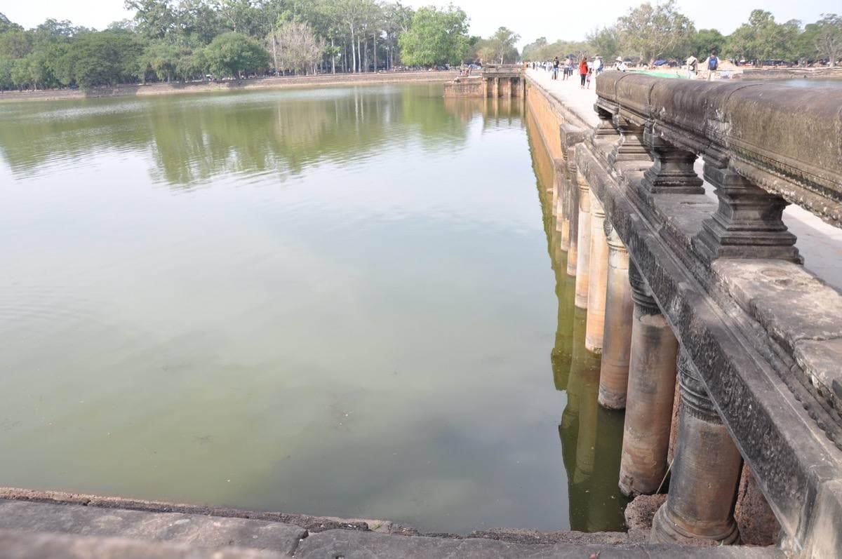 A stone causeway with a carved balustrade running beside a green moat