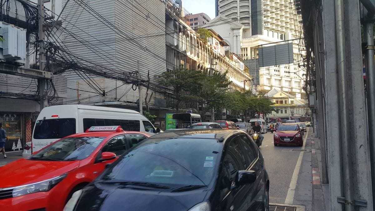 A narrow city road lined with parked cars, shophouses and overhead wires