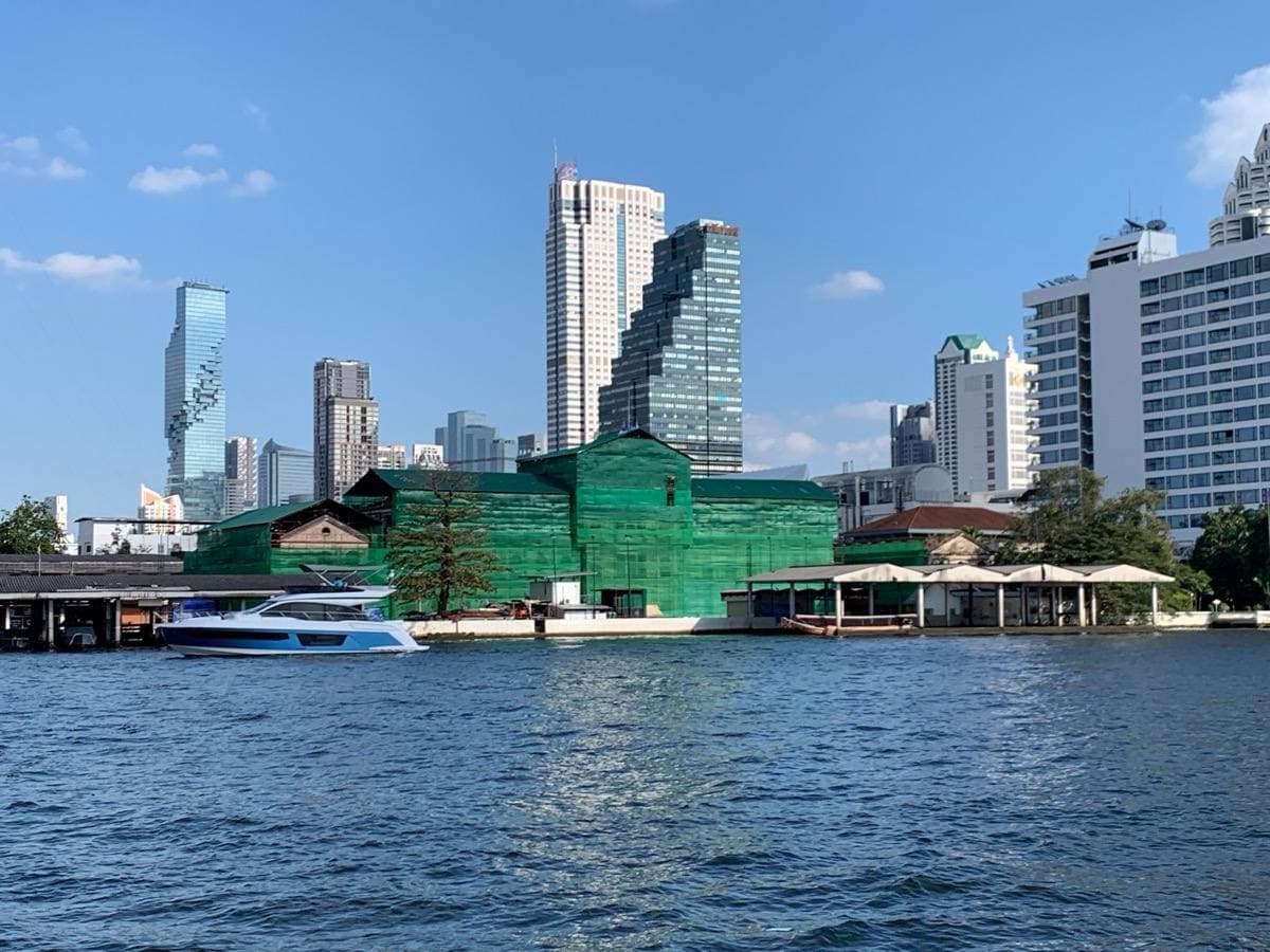 A riverside building wrapped in green scaffolding, high-rises behind