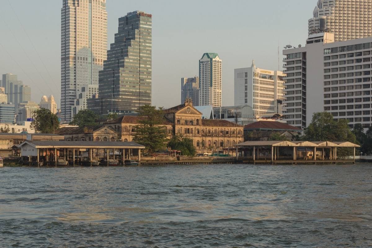 A yellow colonial building on a river bank, towers behind it