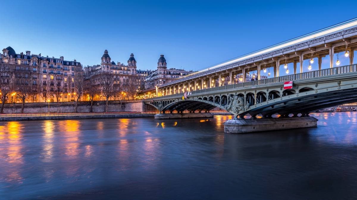 A two-level steel bridge lit up at dusk over the Seine, the metro viaduct on top