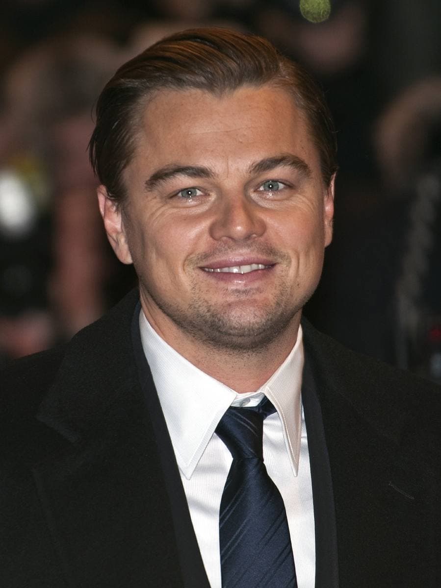 Leonardo DiCaprio in a dark suit and tie, smiling