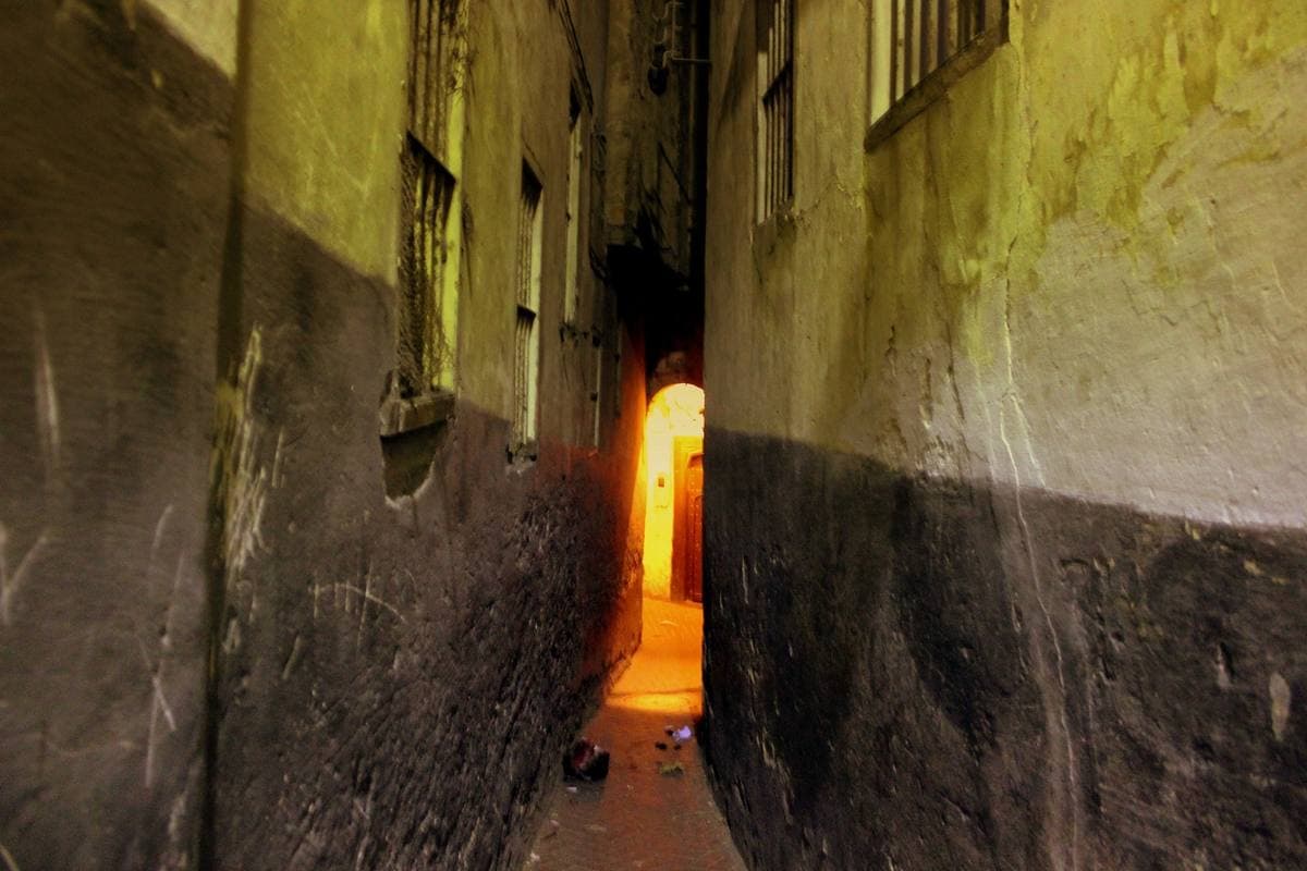 A narrow whitewashed alley lit orange at night, an archway at the end