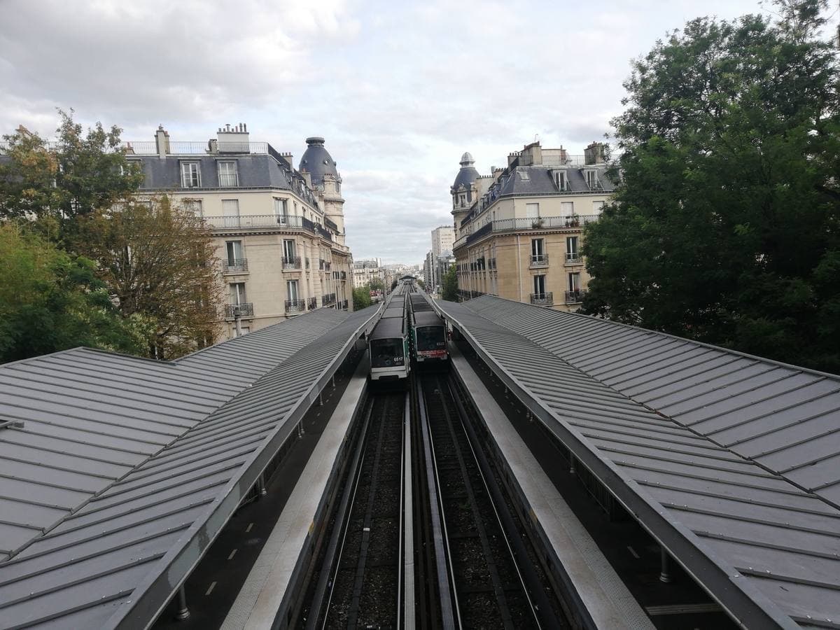 Elevated metro tracks running between grey station canopies towards apartment blocks