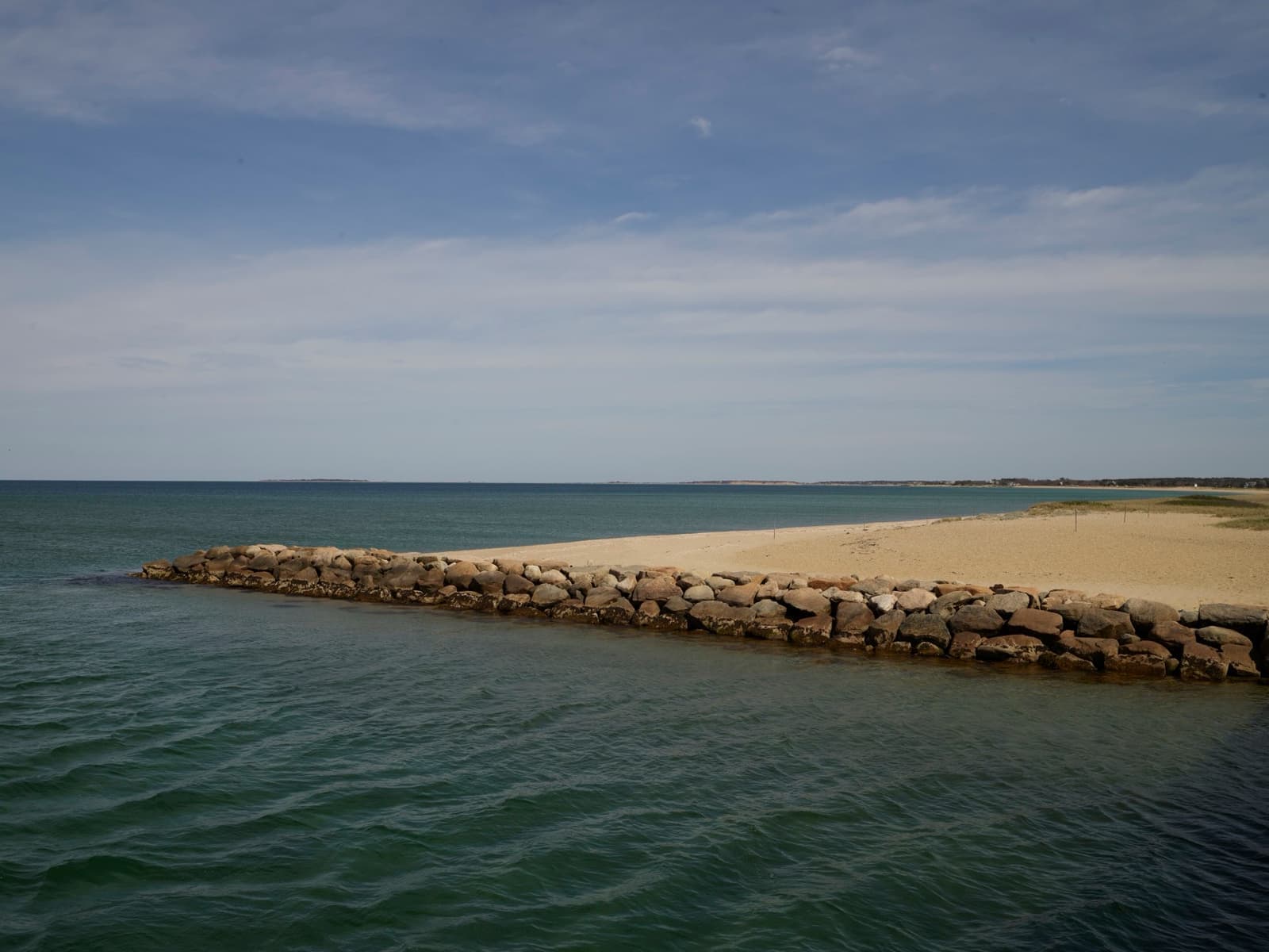 A low stone jetty running into calm water off a sandy point