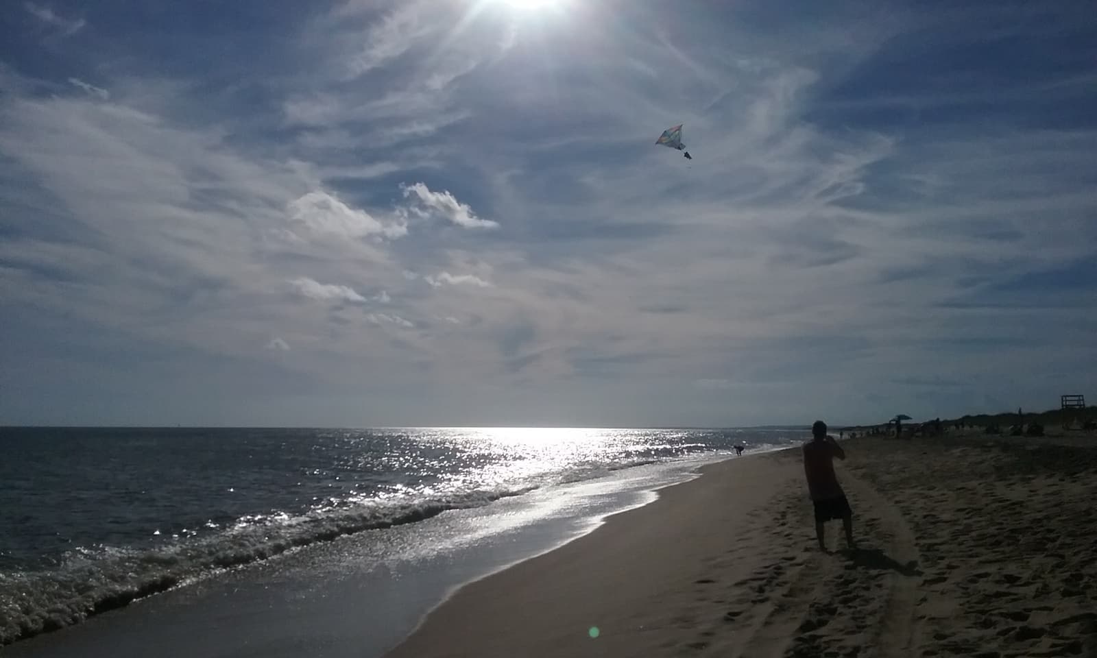 Surf rolling onto a long sandy beach under a bright hazy sky