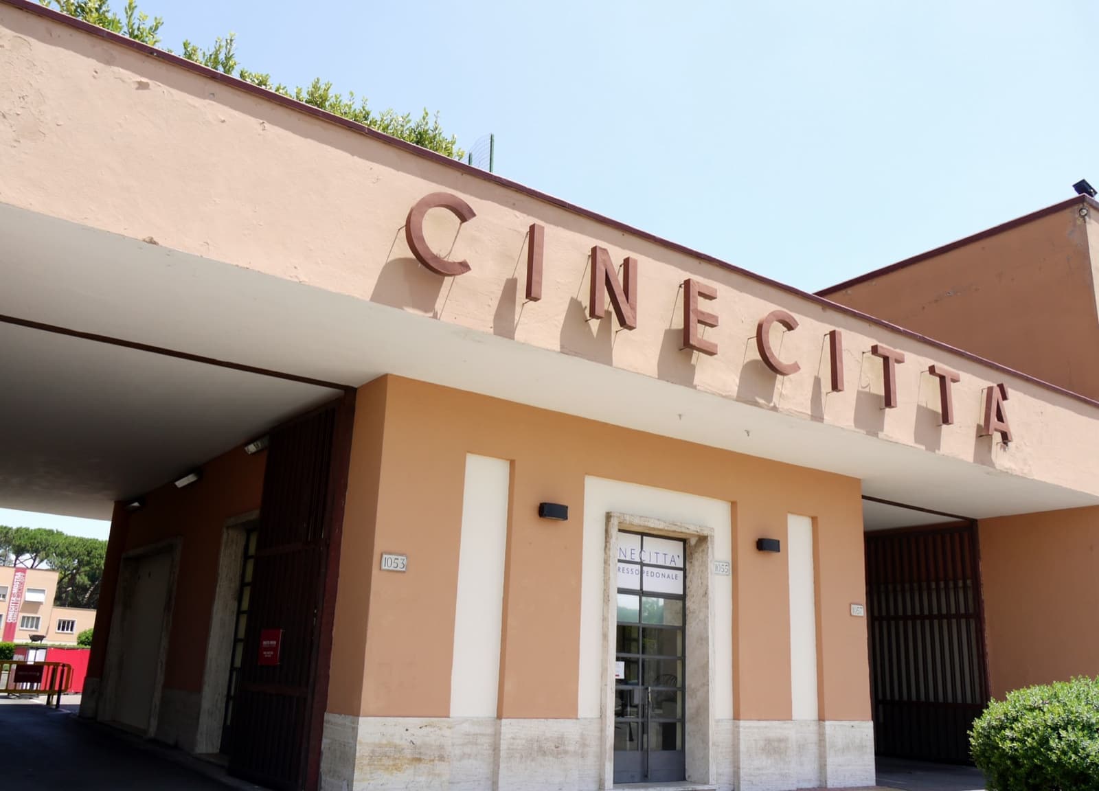 A pale 1930s gatehouse with CINECITTÀ in raised letters