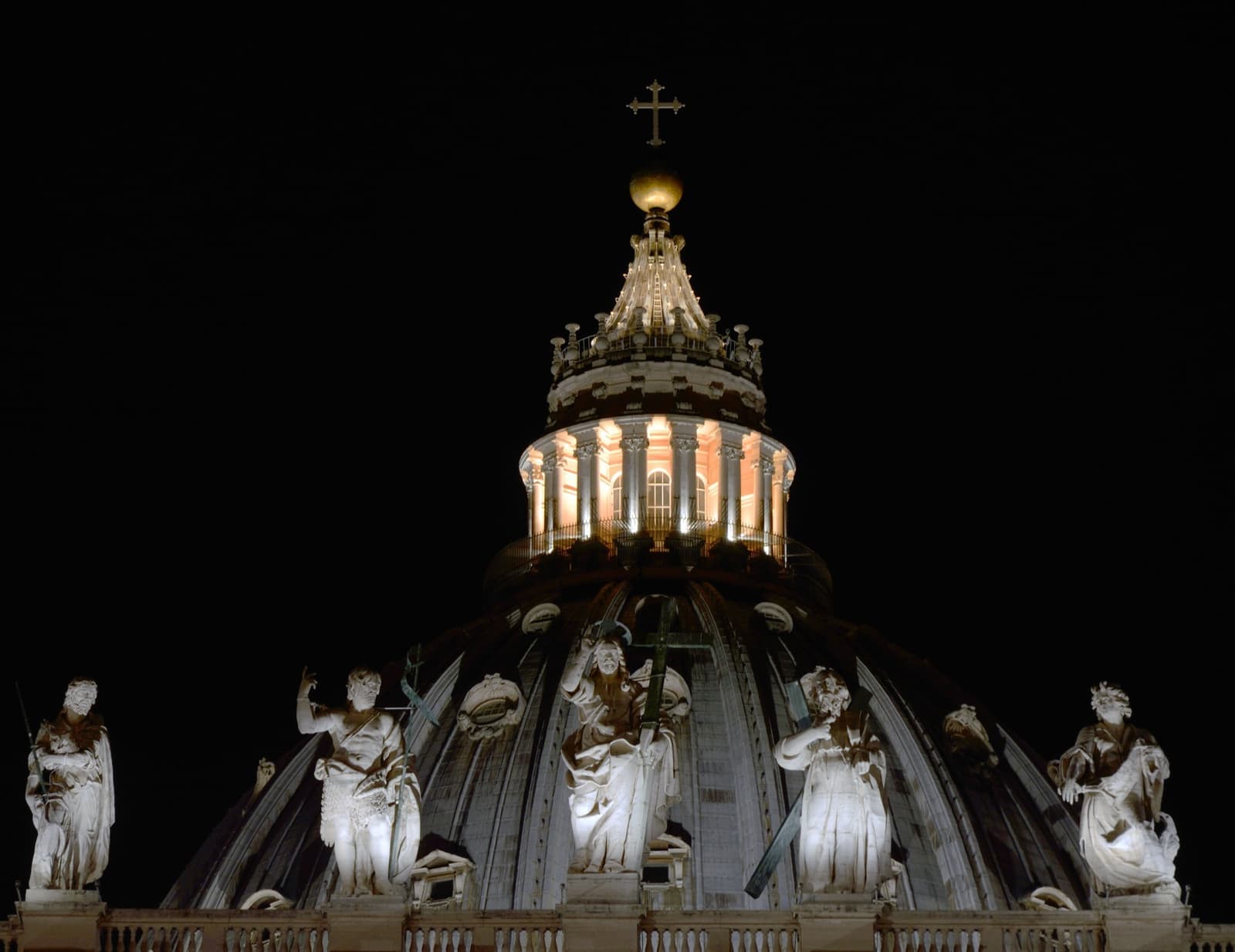 The lit lantern of St Peter’s dome above a row of floodlit statues