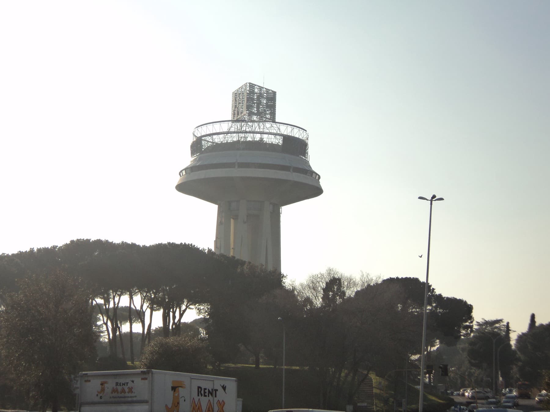 A concrete water tower shaped like a mushroom above pine trees