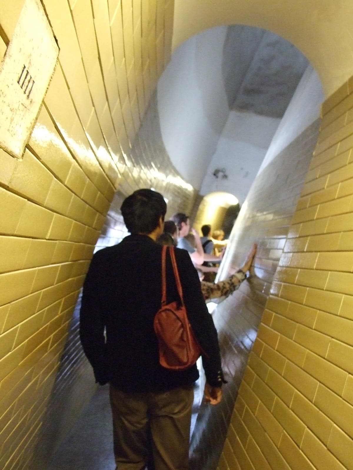 A narrow, leaning, yellow-tiled passage with visitors climbing through it