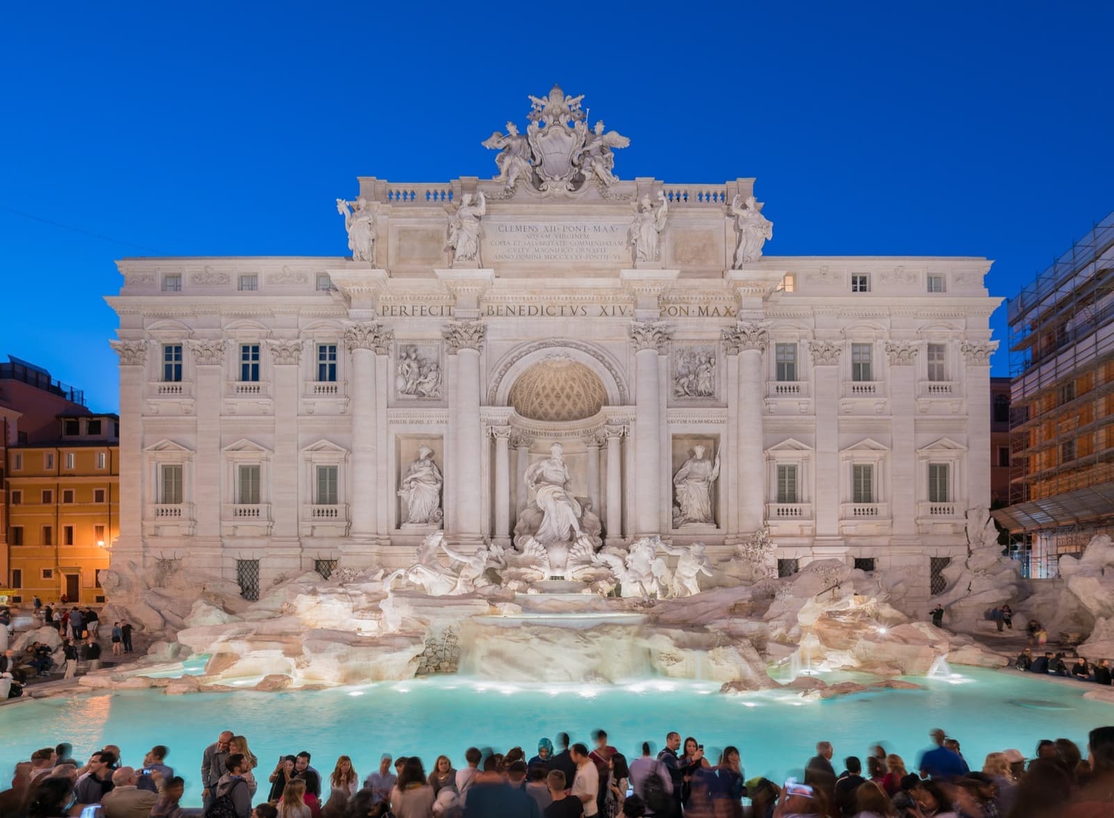 The Trevi Fountain floodlit at dusk, its basin crowded with visitors