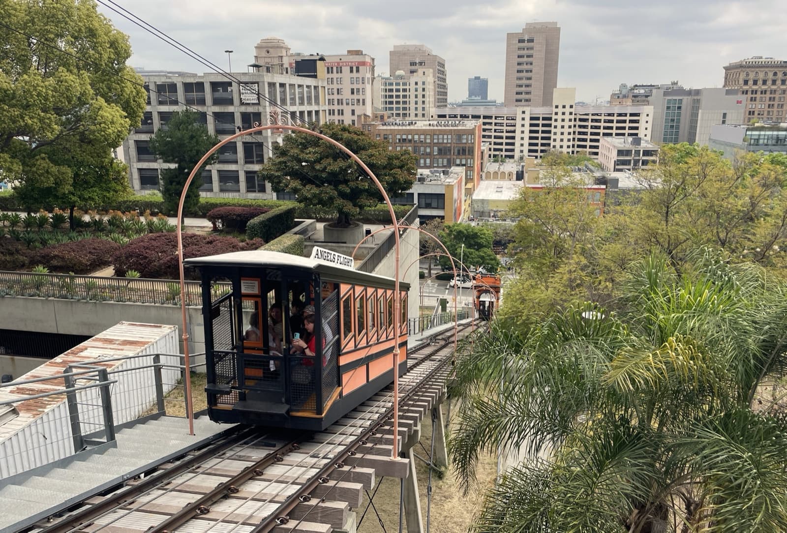 An orange Angels Flight car climbing its track beneath the entrance arch, Downtown towers behind