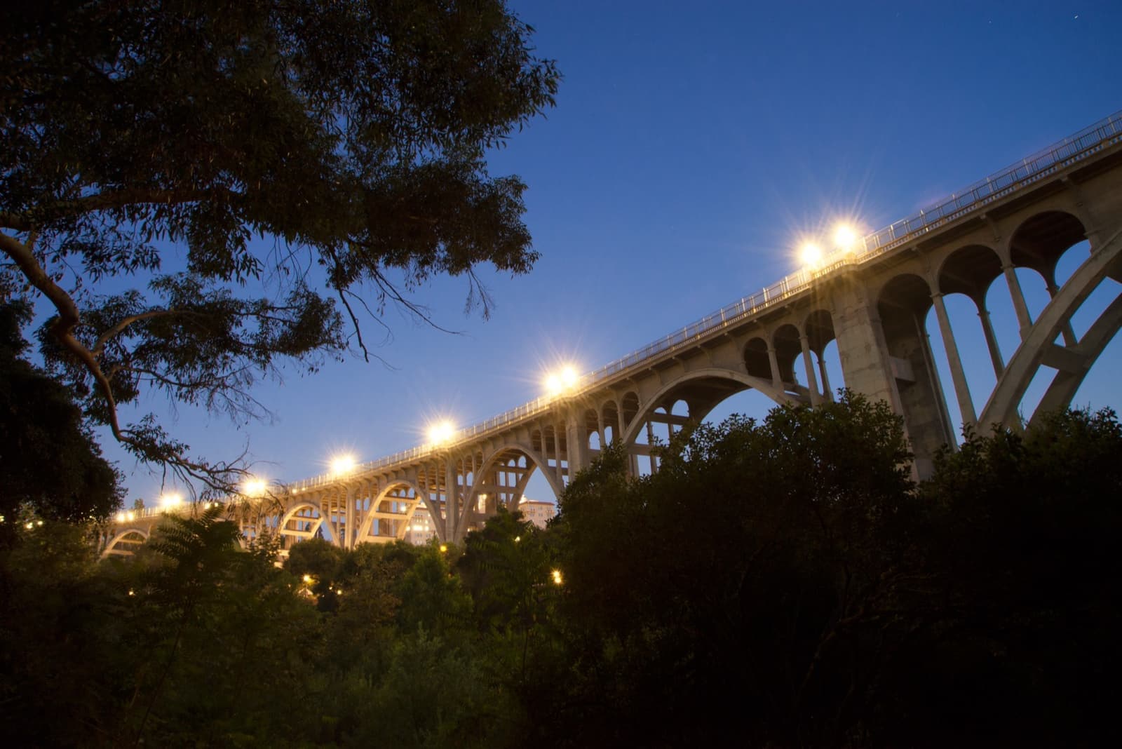 The arched Colorado Street Bridge with its lamps lit against a blue evening sky