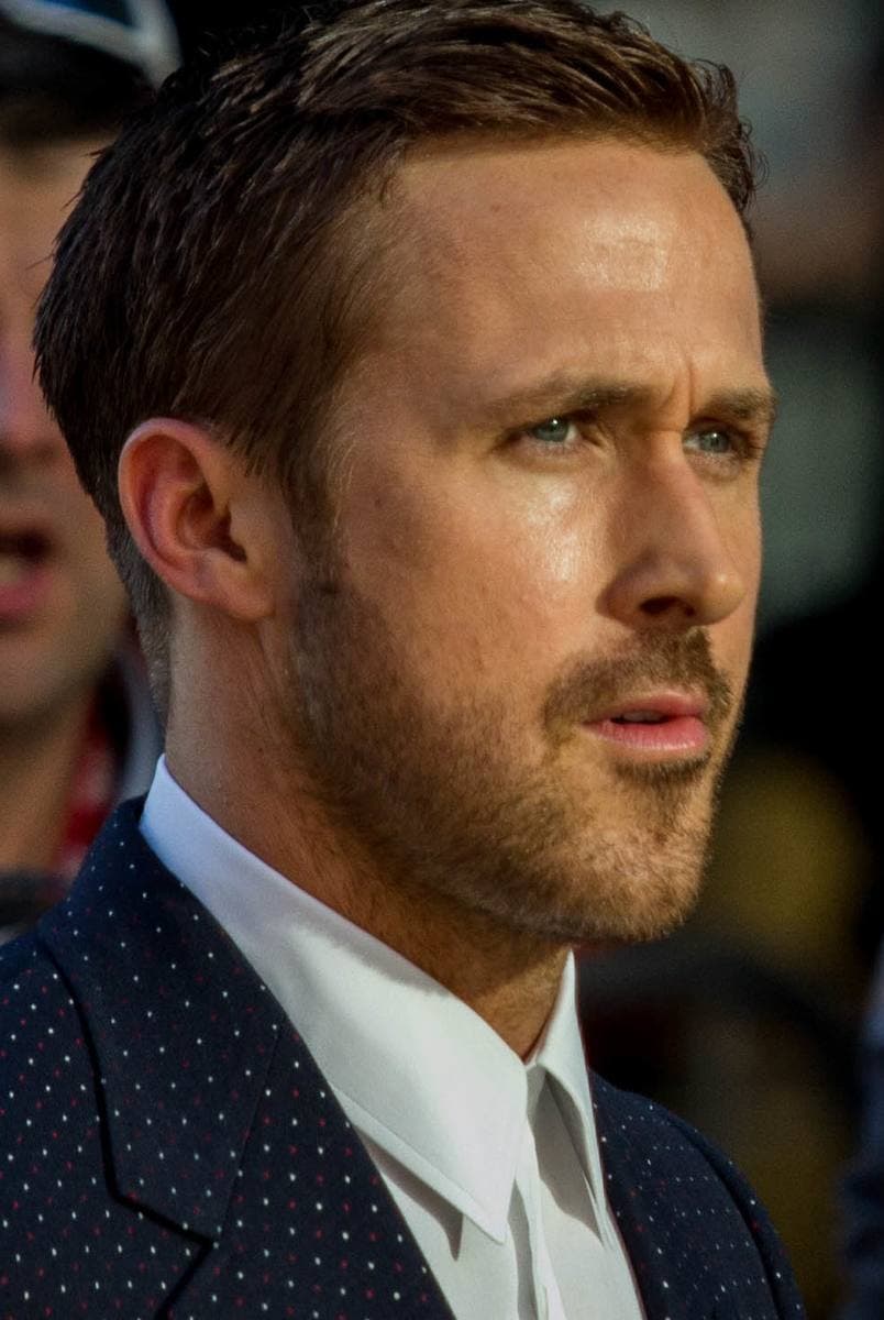 Ryan Gosling in a dark dotted jacket, looking off to one side