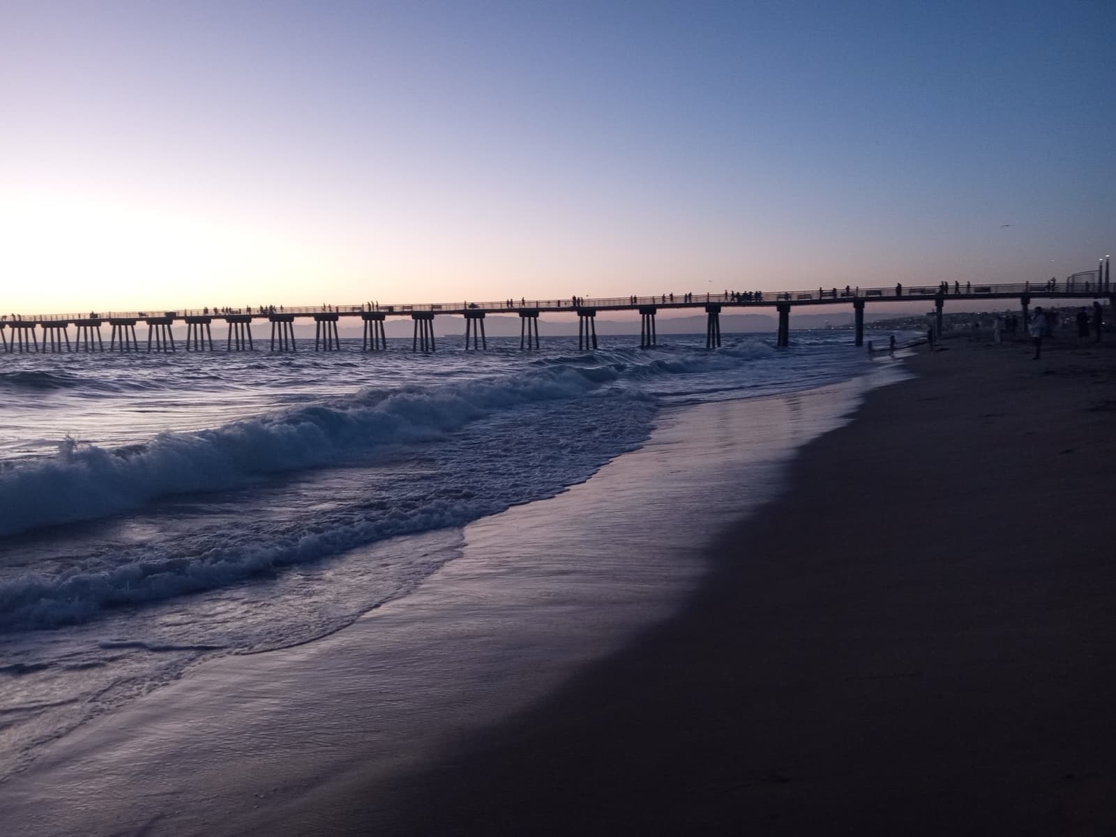 Hermosa Beach Pier in silhouette against a twilight sky, waves breaking in front