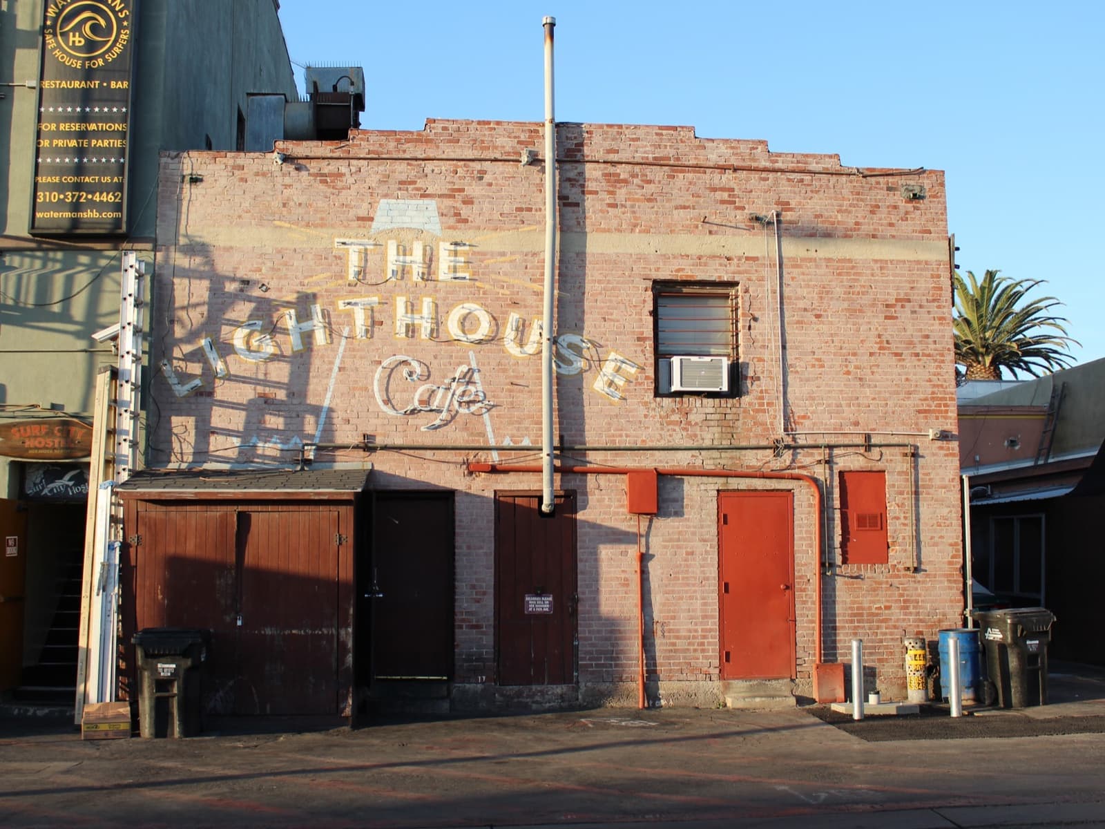 A brick wall painted with the words The Lighthouse Café in late sunlight
