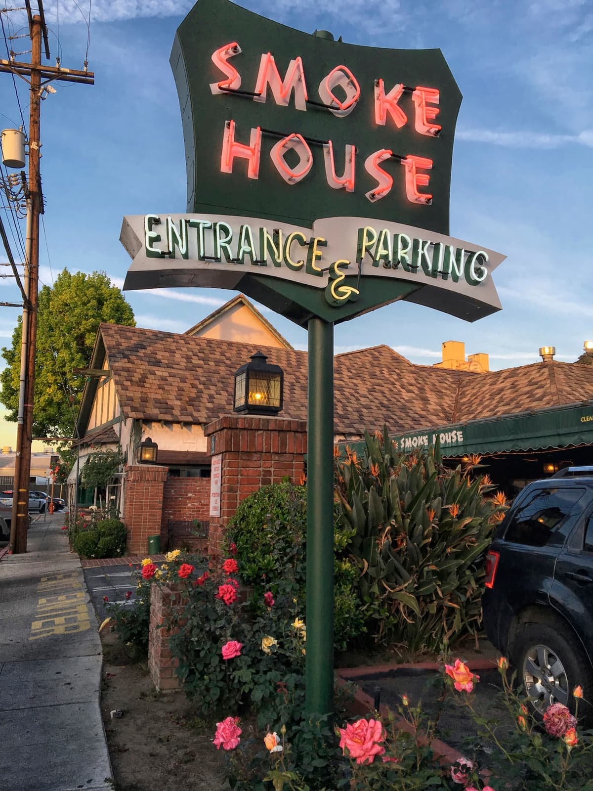 A vintage Smoke House entrance and parking sign above the restaurant and a bed of roses