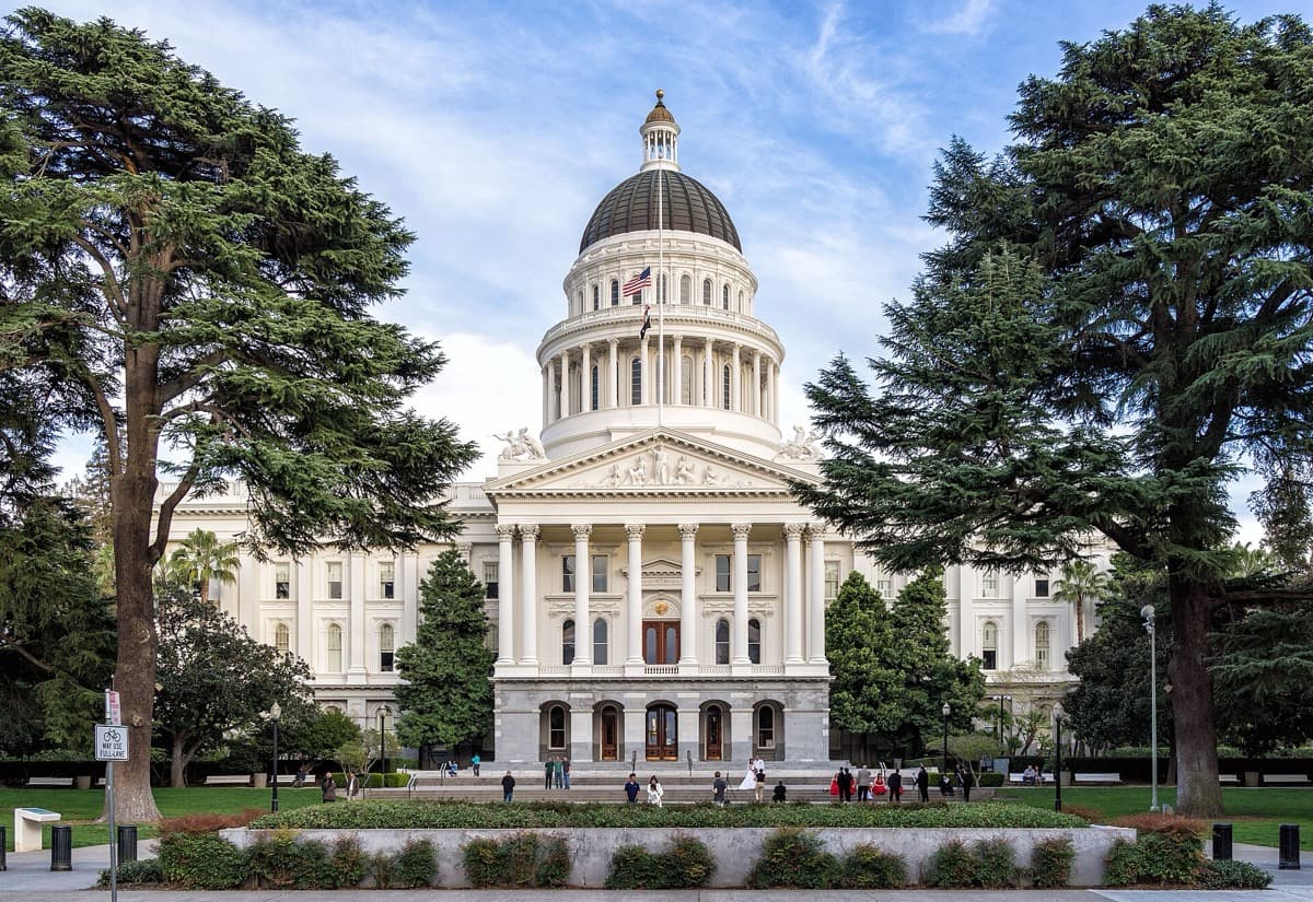 A domed white capitol building behind a tree-lined lawn